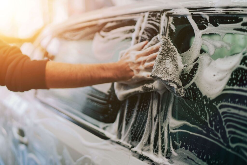 Man washing a soapy car windshield with a grey cloth