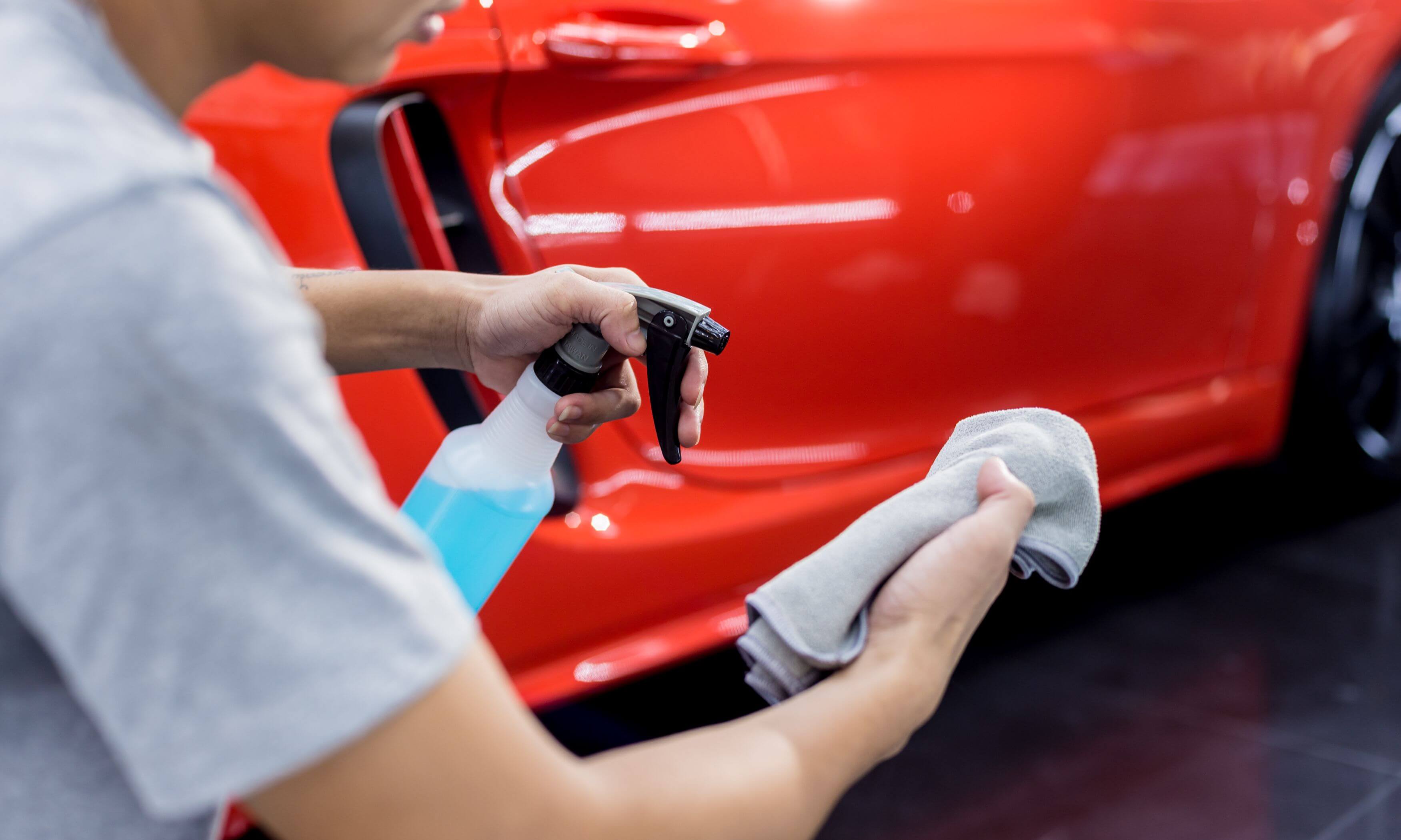 Detailer preparing to clean car by spraying cloth with cleaning solution