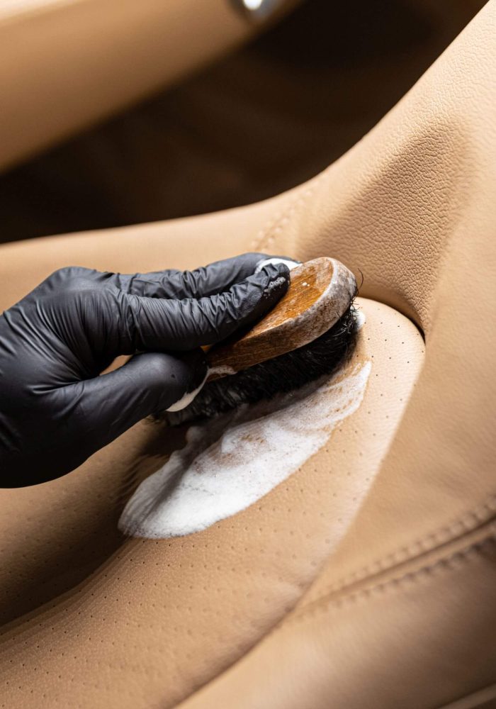 Car detailer cleaning leather seats with soap and brush