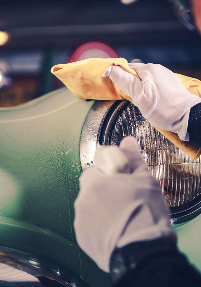 Detailer cleaning the headlight of a vintage green automobile