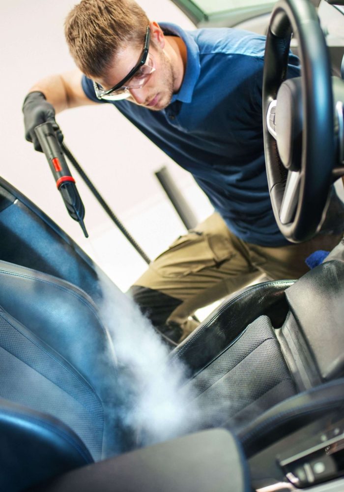 Man cleaning the front seat of a vehicle with steam